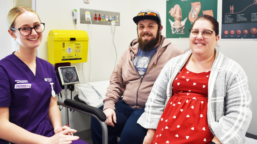 A male and pregnant female sitting on a bed in a consult room.