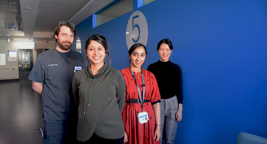 Four healthcare professionals stand in a hospital corridor near a sign with the number 5.