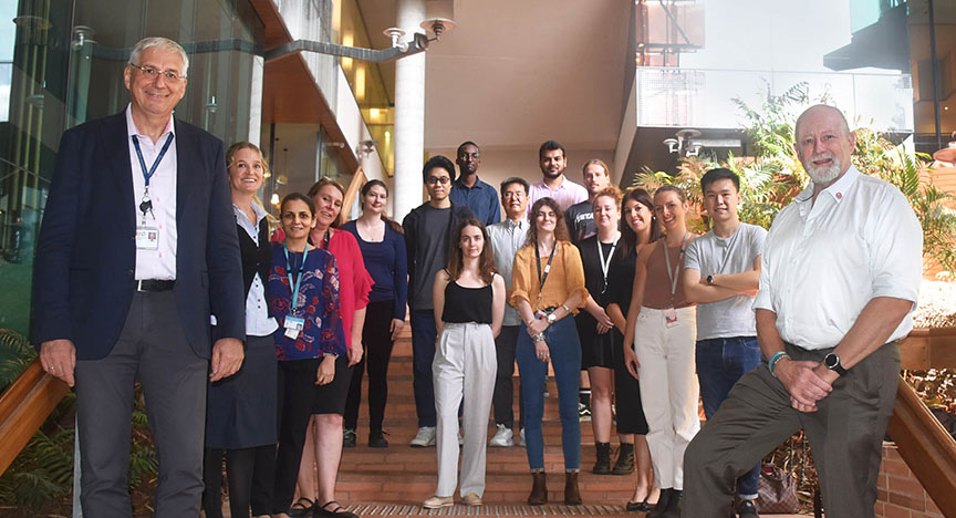 A group of people stands on stairs inside a building, posing for a photo. The setting appears to be a professional or academic environment.