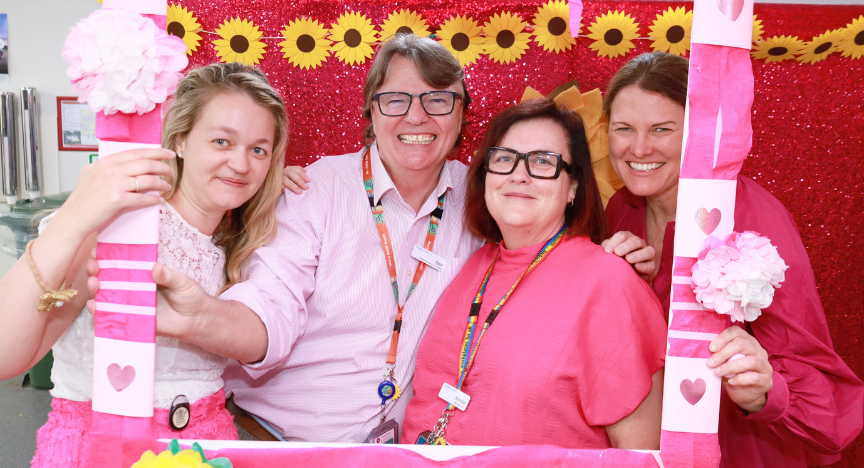 Four people pose together at a festive event with pink and red decorations, including flowers and hearts.