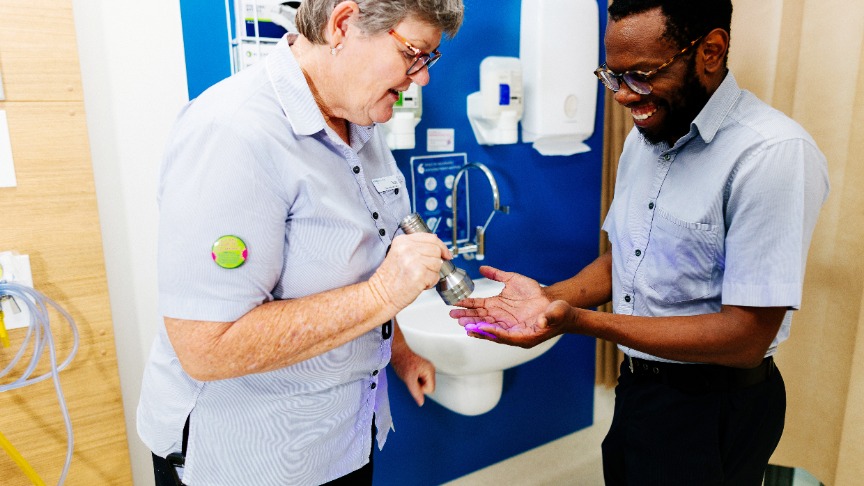 Clinical Nurse shines UV light on male nurses hands to test effective hand washing