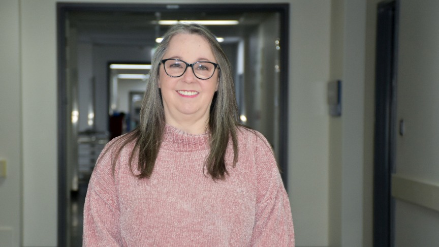 Femal midwife wearing a pink jumper standing in a hospital hallway