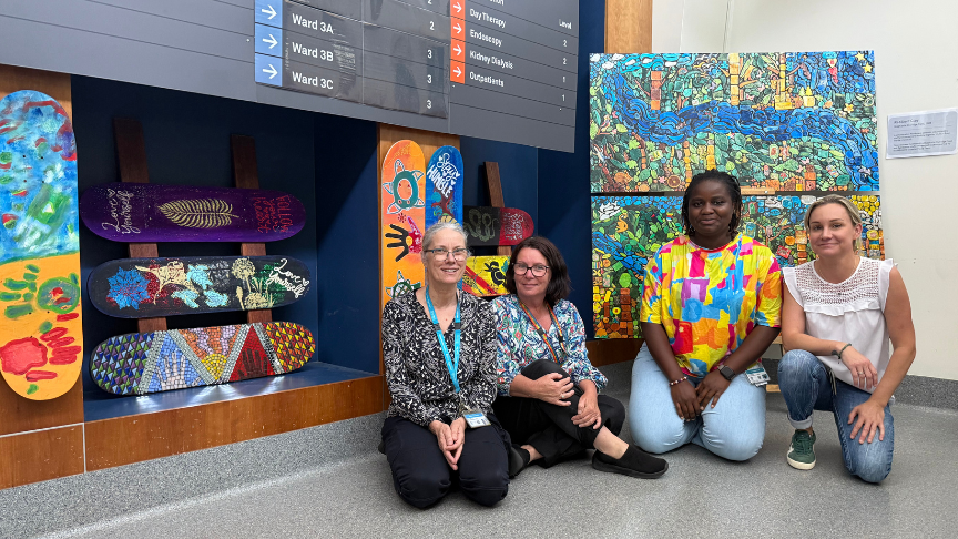 Four women, mental health staff, pose in front of a vibrant wall of skateboards, smiling and showcasing their support for wellness