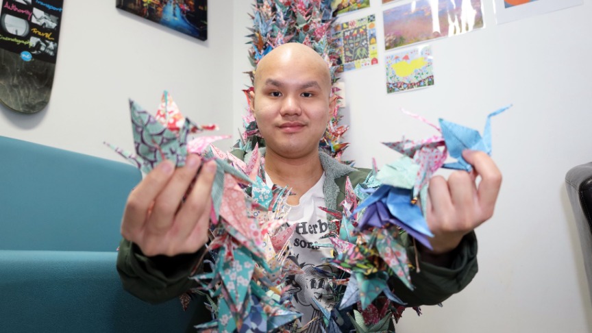 Ryan, a cancer patient, proudly holds a colourful origami paper crane he created