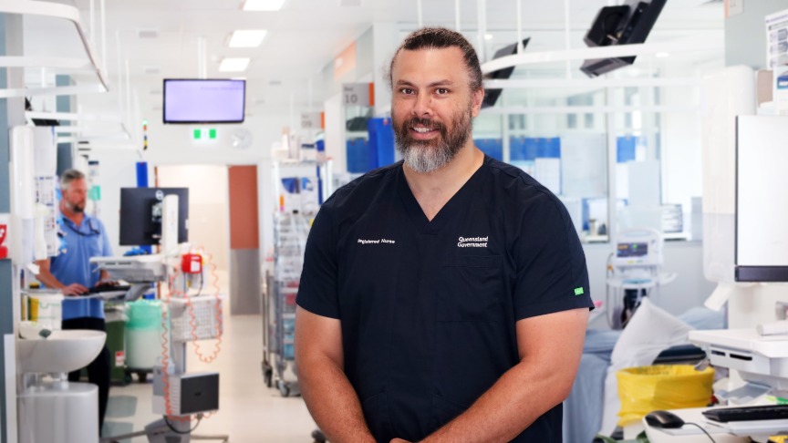 Nurse Franc Gilbert stands in a hospital corridor, wearing scrubs and a name badge, ready to assist patients