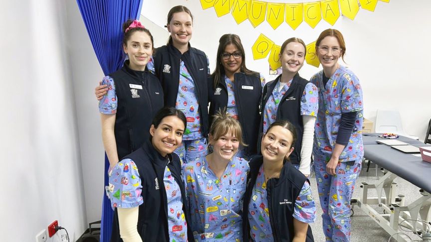 8 health professionals in fun scrubs, first row kneeling