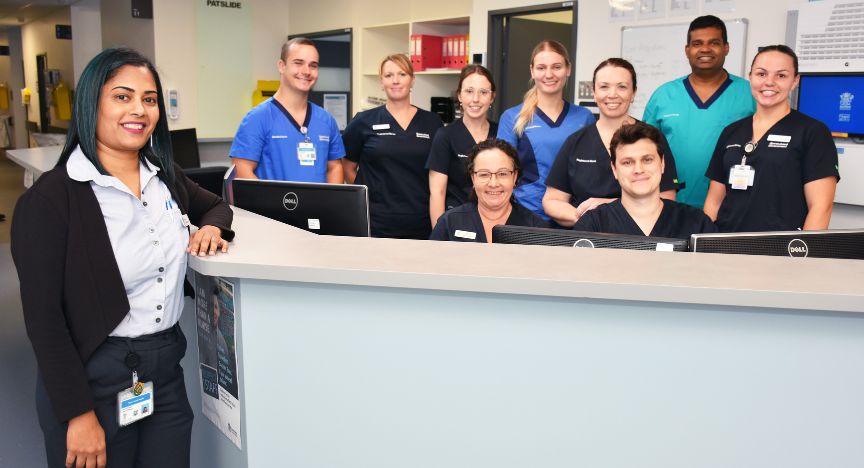 Ten healthcare workers in a hospital setting, standing in front and behind a ward counter