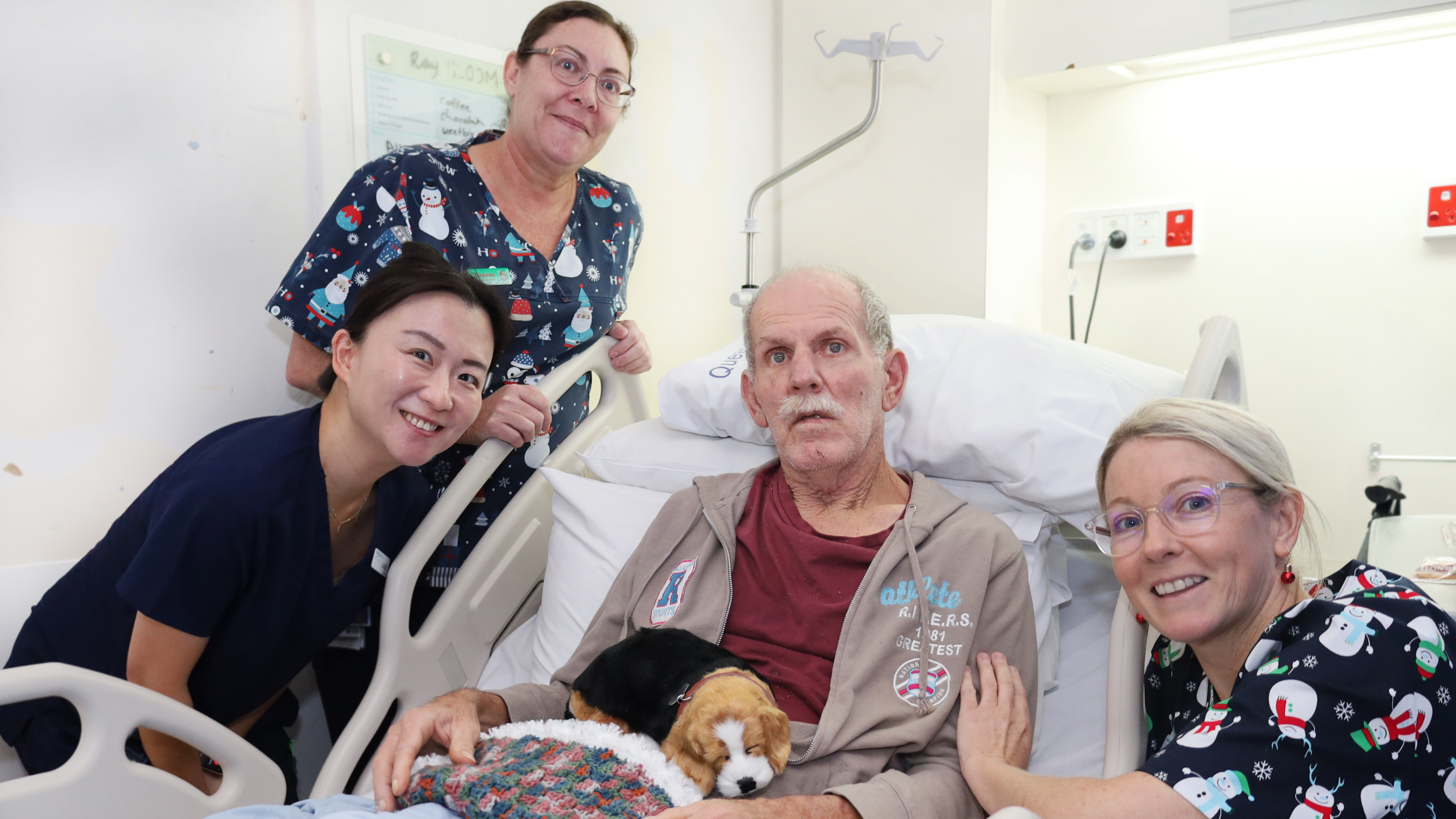 patient in bed, therapy dog on lap, surrounded by 3 nurses