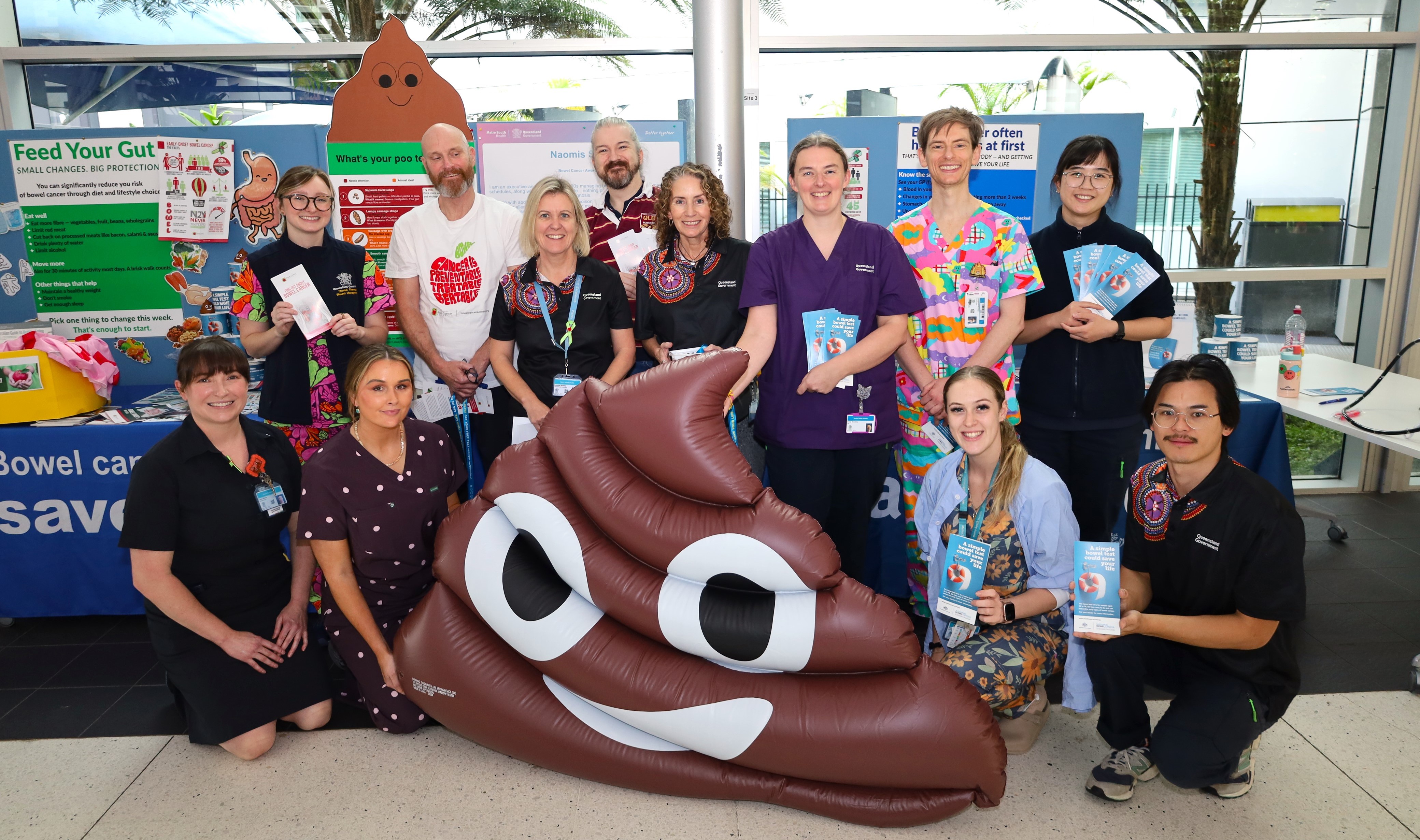 A group of people smiling and posing playfully with a large, cartoonish poop sculpture