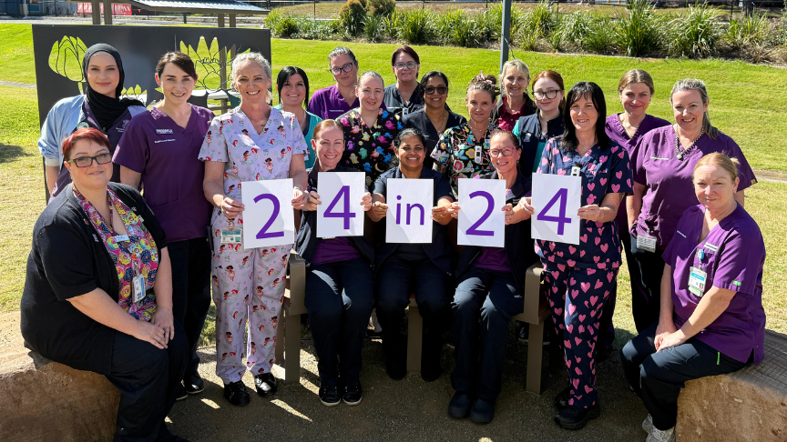 Large group of midwives and nurses, most in purple scrubs holding up signs that read 24 in 24
