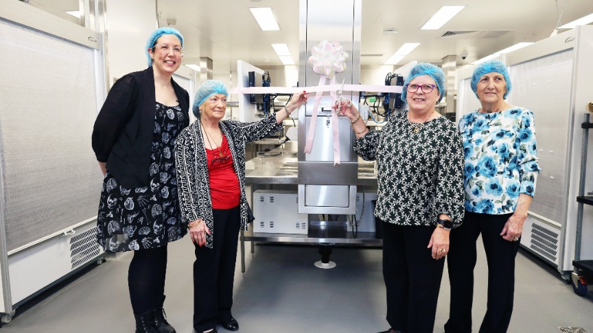 Retirees smiling, cutting ribbon in hospital kitchen