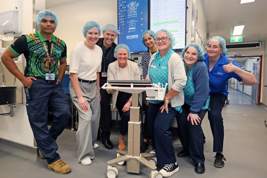 A diverse group of dietitians and kitchen staff wearing hairnets stand near the hardware for room service on demand