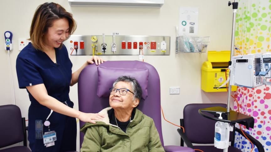 A nurse in scrubs smiling down at a patient in a purple chair