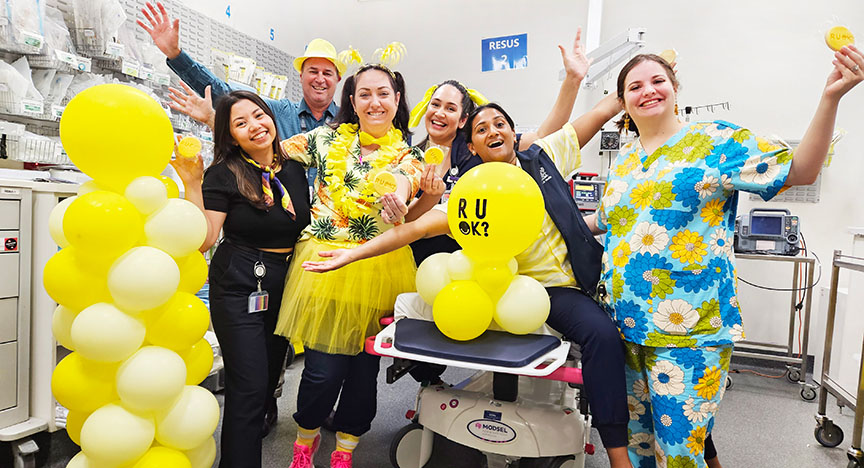 Healthcare staff in colorful outfits and yellow accessories celebrate R U OK? Day in a hospital, promoting mental health awareness.