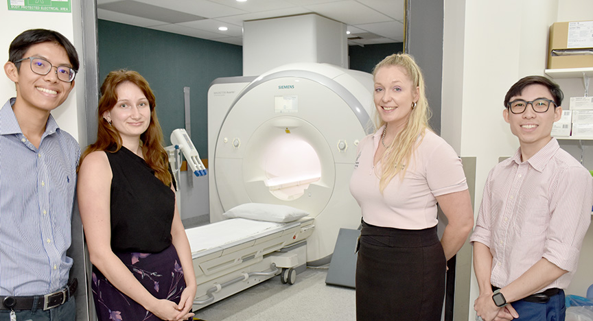 Four people stand in front of an MRI machine in a medical facility, highlighting collaboration in cardiology.