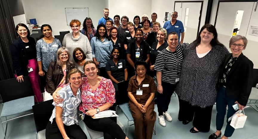 A group of healthcare professionals at Logan Hospital, including First Nations staff, gathered in a room for a meeting or event.