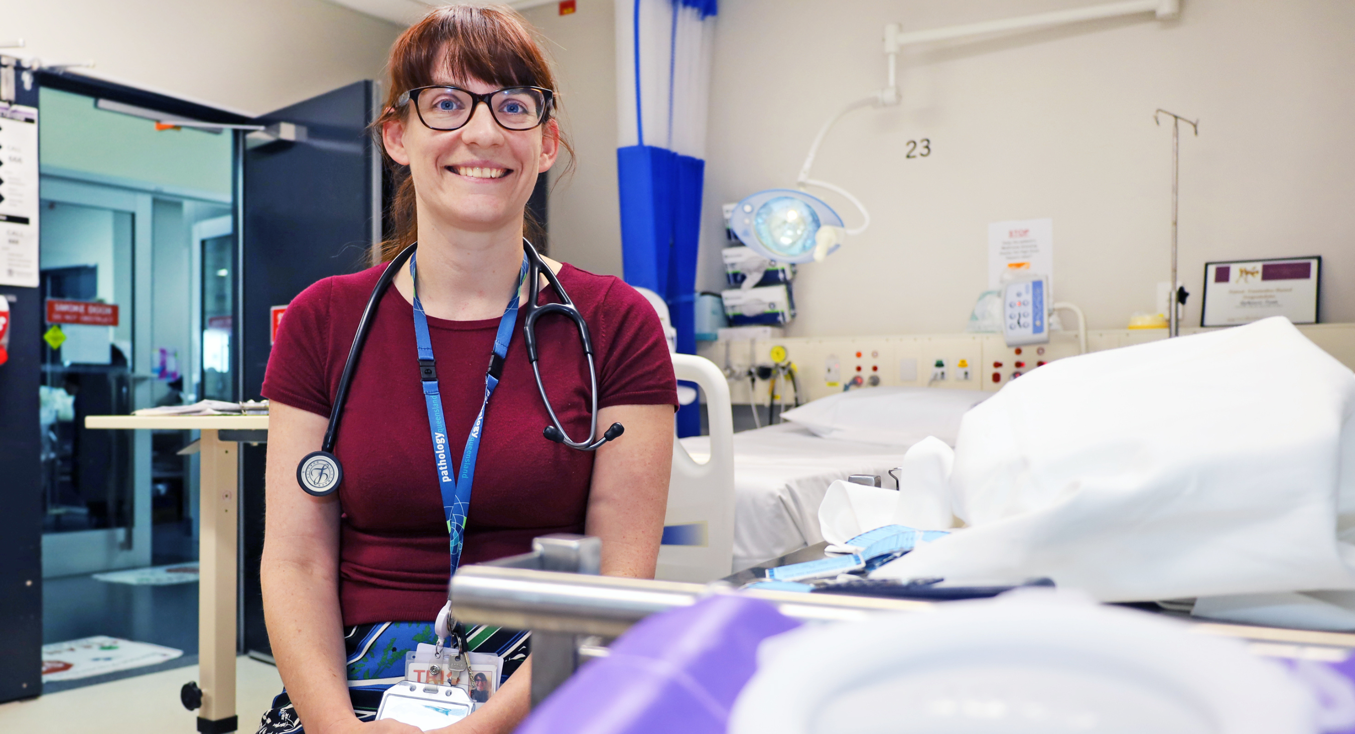 Female doctor sitting on bed in hospital room, smiling