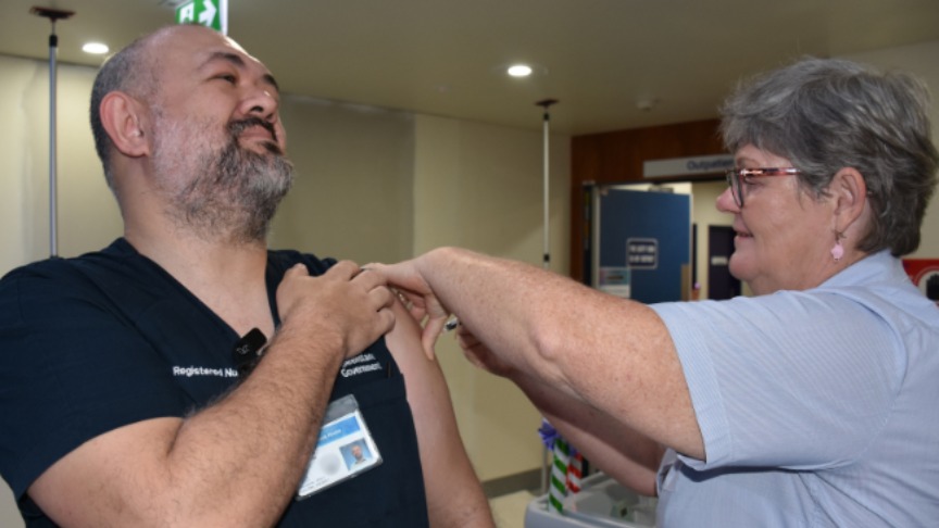 Male Nurse with sleeve rolled up receives a flu injection from another nurse