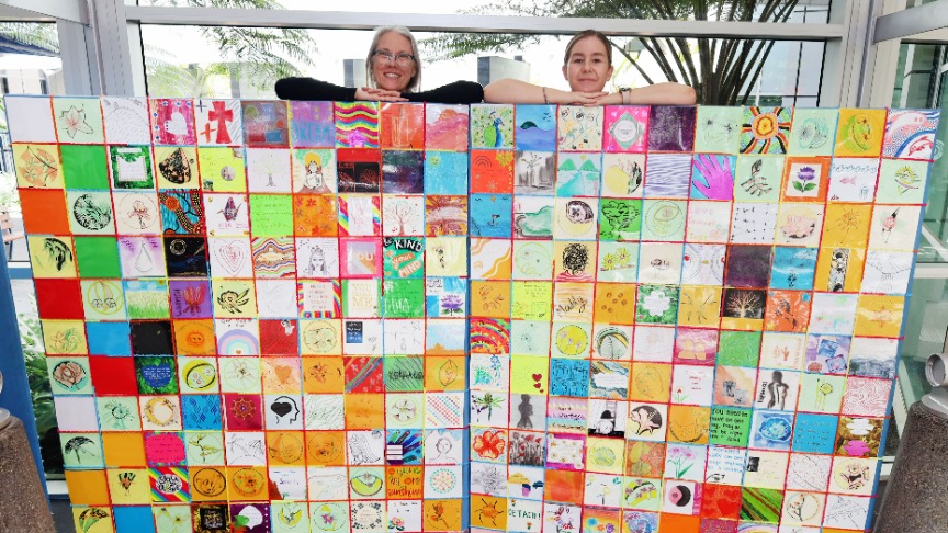 two female staff members smiling behind large wall of art