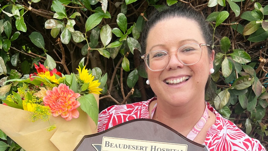 Headshot of a female wearing a bright dress and clear glasses, holding flowers and a trophy