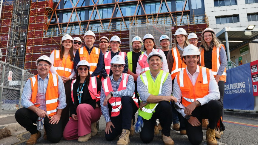 Team of expansion staff wearing hard hats and vests in front of a hospital, engaged in planning discussions