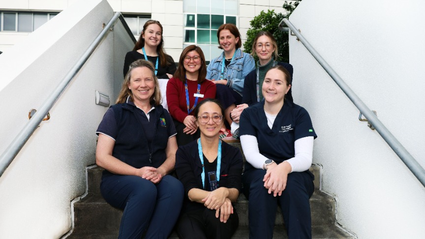 A group of women from allied health staff seated on steps in front of a hospital building