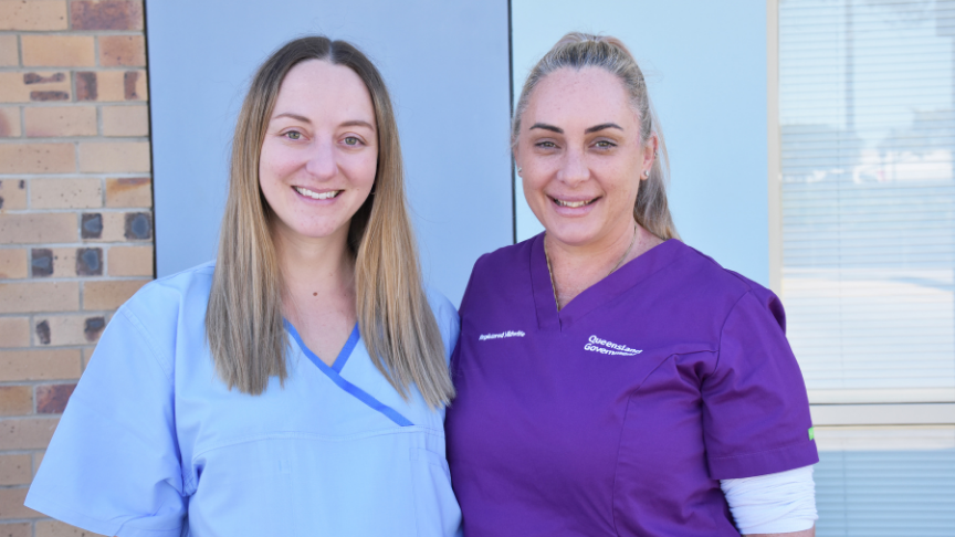 A doctor and a midwife standing together. One is wearing blue scrubs, the other purple scrubs