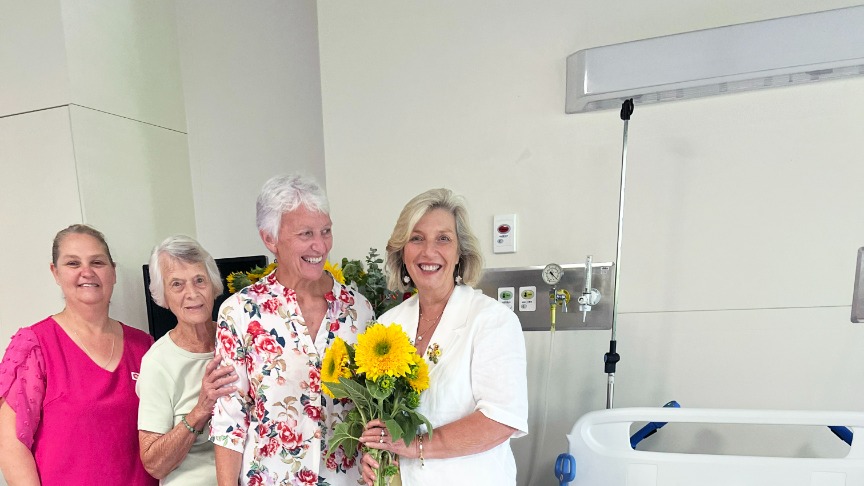 A group of women standing around a hospital bed that has a sunflower quilt on it