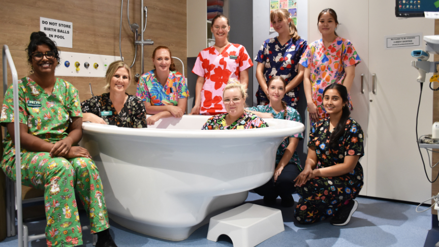 Group of midwives in colourful scrubs standing around a birthing pool