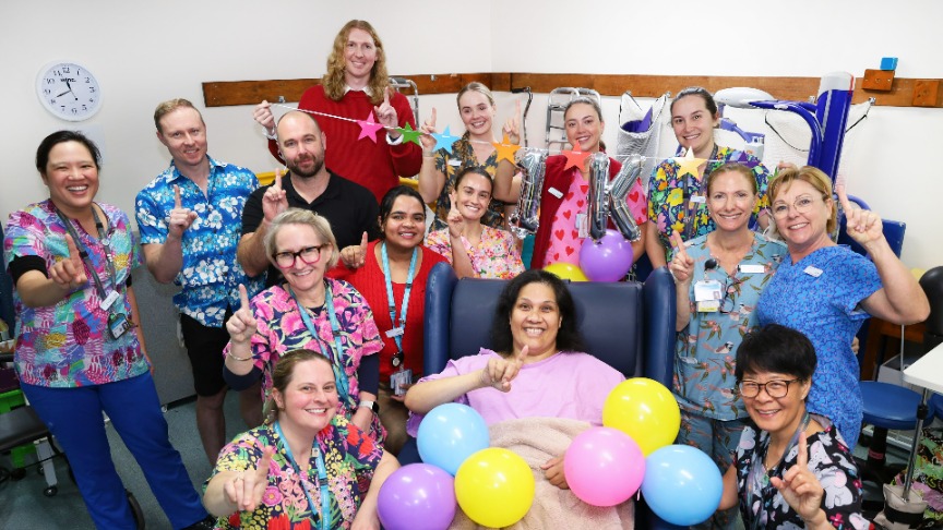 A group of rehab staff in scrubs poses with balloons to celebrate their 1000th patient milestone