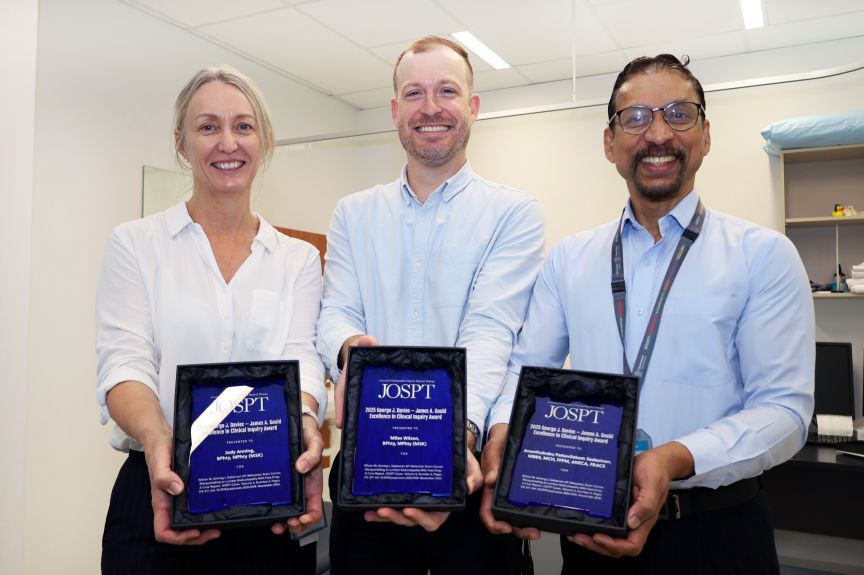 Three healthcare professionals from the Back Assessment Clinic showcase their awards in a bright, organized room