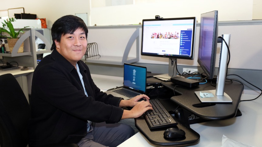 Graduate officer Ian Zhong working at his desk, focused on his computer and keyboard