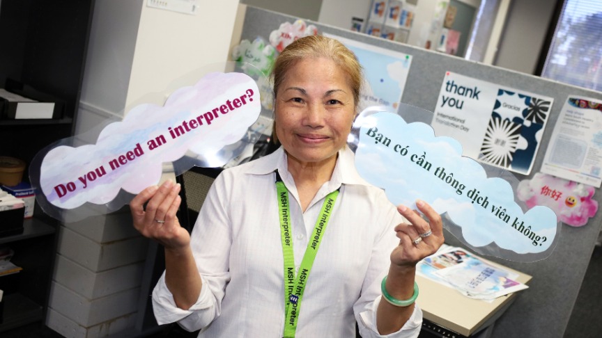 A woman named Yen holds two signs asking, 'Do you need an interpreter?' to assist with communication needs