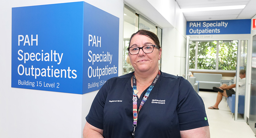 A nurse stands in front of the PAH Specialty Outpatients sign in a hospital corridor.