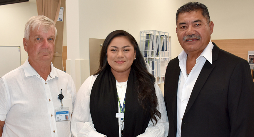 Three people standing together in a professional setting, one wearing a lanyard and ID badge. They appear to be in a healthcare environment.