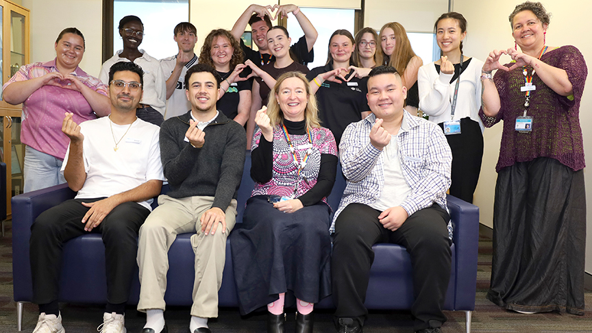 A group of young people sitting at a couch and making a heart sign with their hands