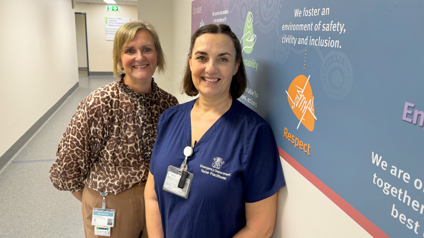 Two women smiling at the camera while standing in a hallway