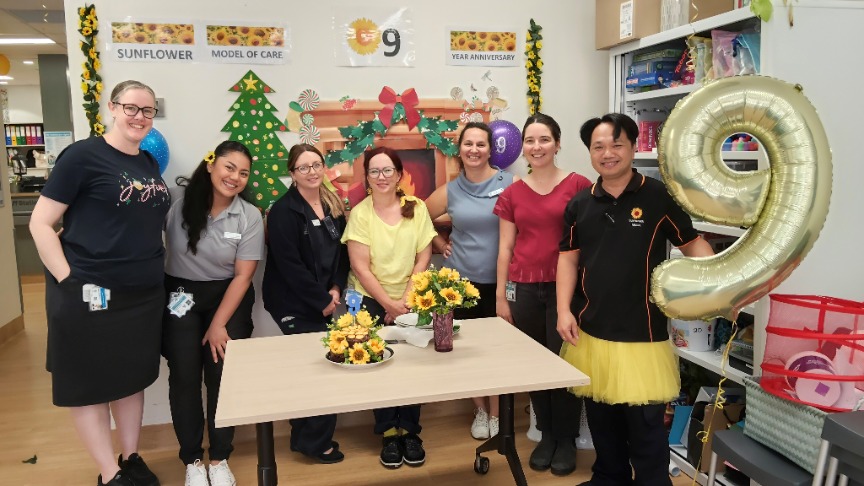 A group of people standing behind a decorated table, one holding a 9 balloon 