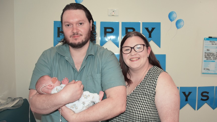 A man holding a baby with his wife standing next to him
