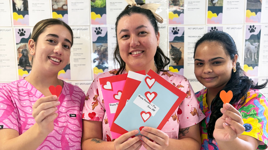 Three nurses in fun scrubs holding love hearts and a card up to the camera