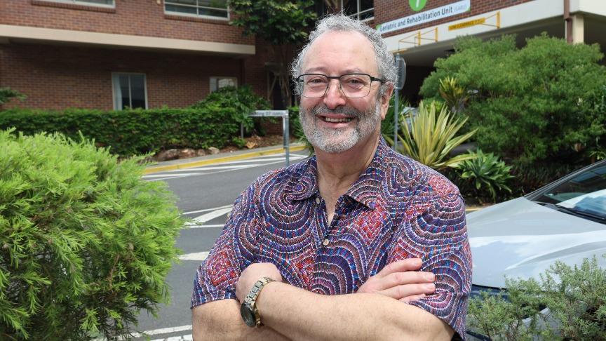 An experienced male doctor with a beard and glasses standing outside the Geriatric and Rehabilitation Unit at PA Hospital