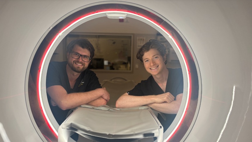 Two male radiographers looking through CT Scanner