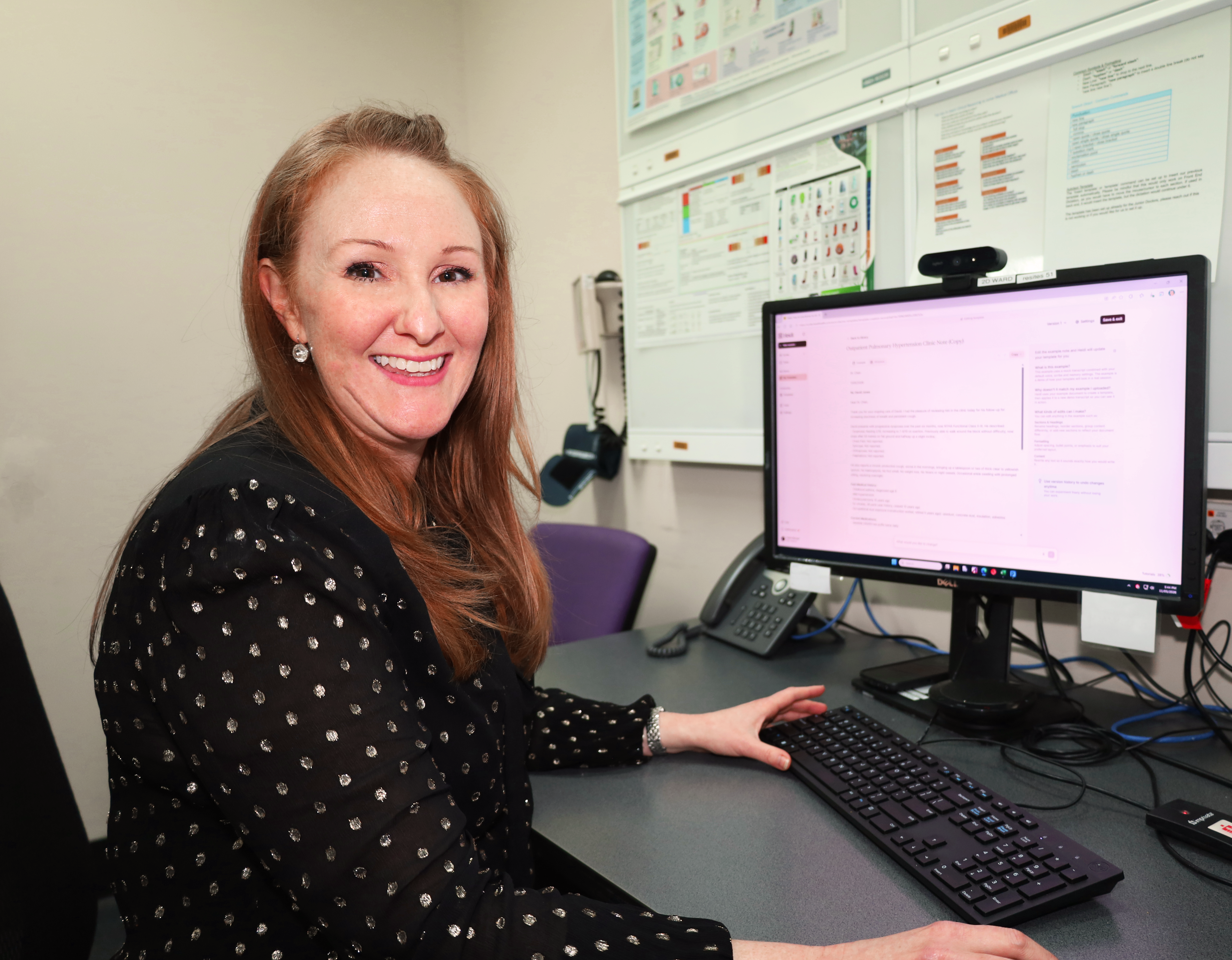 A doctor smiles at the camera. Behind her is Heidi Ambient AI Scribe displayed on a computer screen.