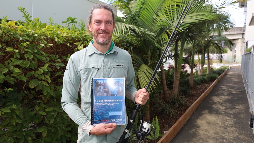 man holding fishing rod and fishing booklet outdoors