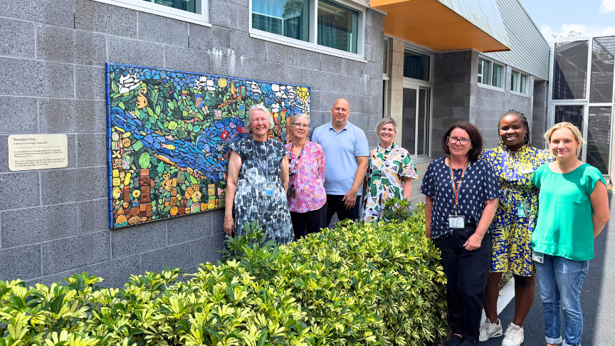 A group of mental health staff stand in front of a building featuring a colorful mosaic artwork on its exterior