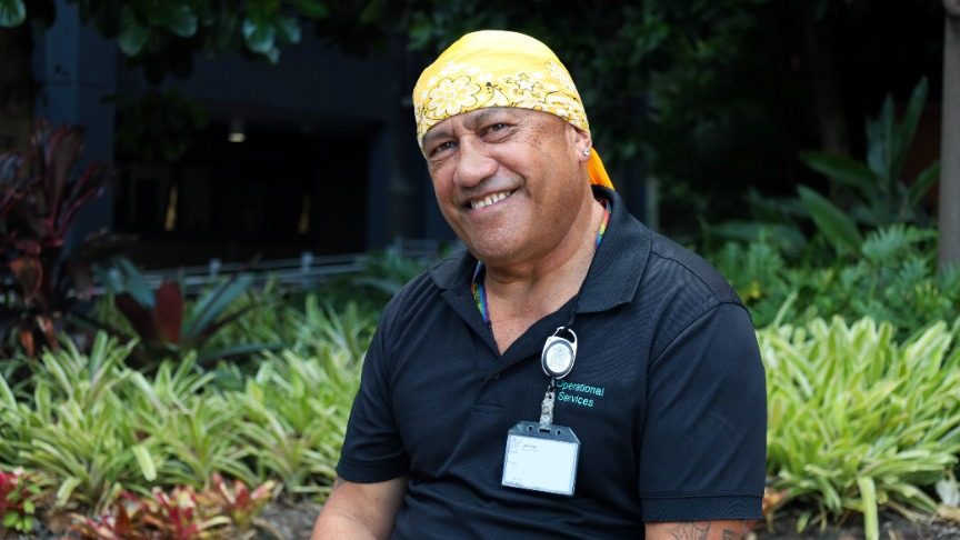 Lonnie Puru, a PA staff member, sits in front of plants wearing a yellow bandana