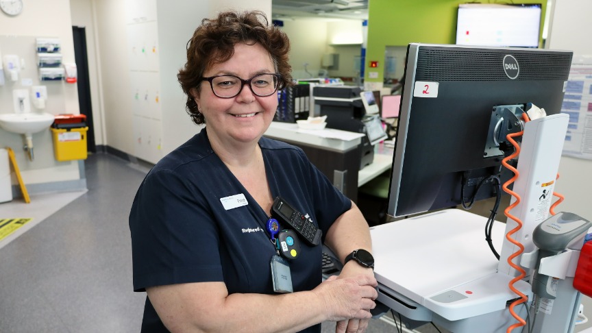 A female nurse leader smiling at the camera in a surgical setting alongside digital equipment used at PA Hospital
