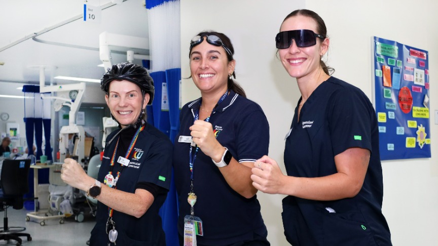 Three women dressed in scrubs stand in a hospital corridor, preparing for a triathlon as dedicated ICU nurses