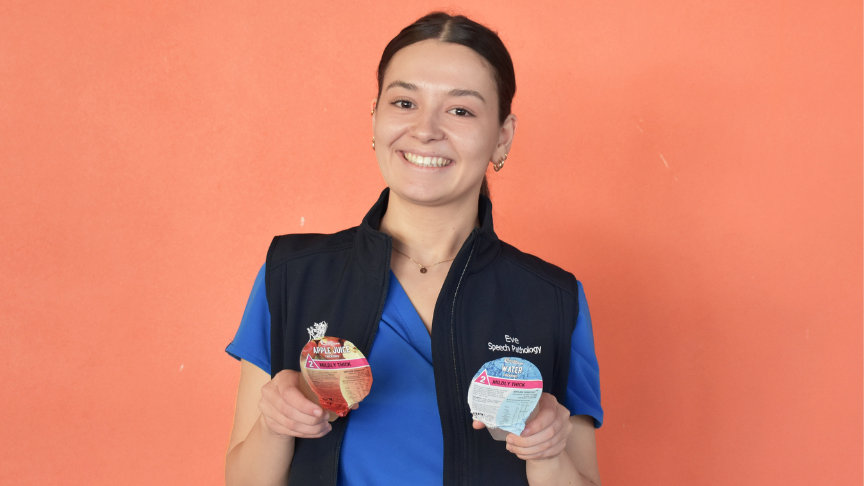 Young woman holding thickened fluids in front of a coral coloured wall