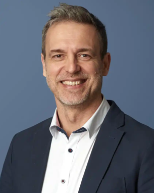 Head and shoulder image of a man with short brown hair in a white shirt with a navy suit jacket